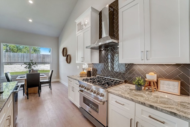 kitchen with appliances with stainless steel finishes, vaulted ceiling, wall chimney range hood, light hardwood / wood-style flooring, and white cabinets