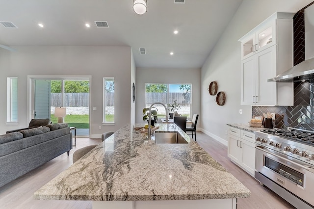 kitchen featuring a wealth of natural light, sink, wall chimney range hood, high end stove, and a kitchen island with sink