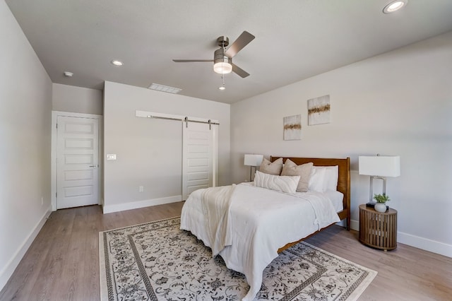 bedroom with ceiling fan, a barn door, and light hardwood / wood-style floors