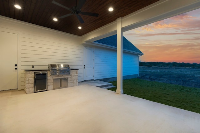 patio terrace at dusk featuring a grill, ceiling fan, and an outdoor kitchen