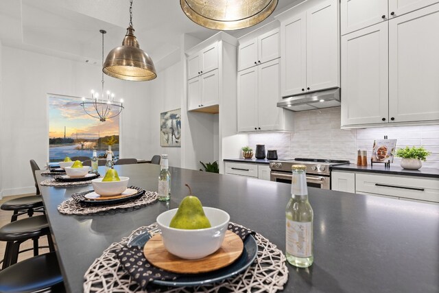 kitchen with stainless steel stove, decorative backsplash, white cabinets, a kitchen bar, and decorative light fixtures