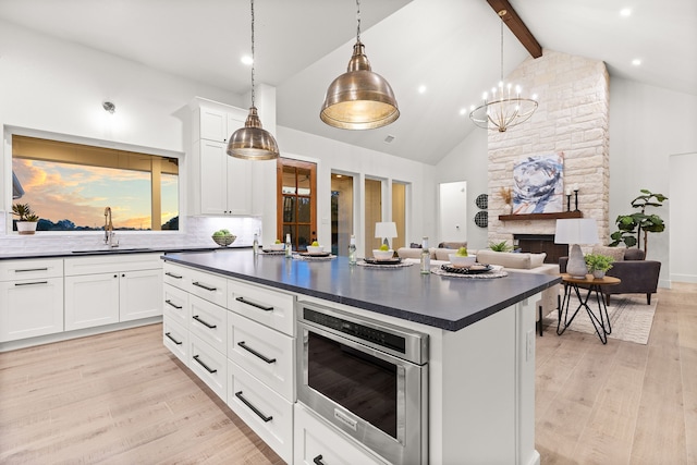 kitchen featuring stainless steel microwave, beamed ceiling, sink, white cabinets, and decorative backsplash