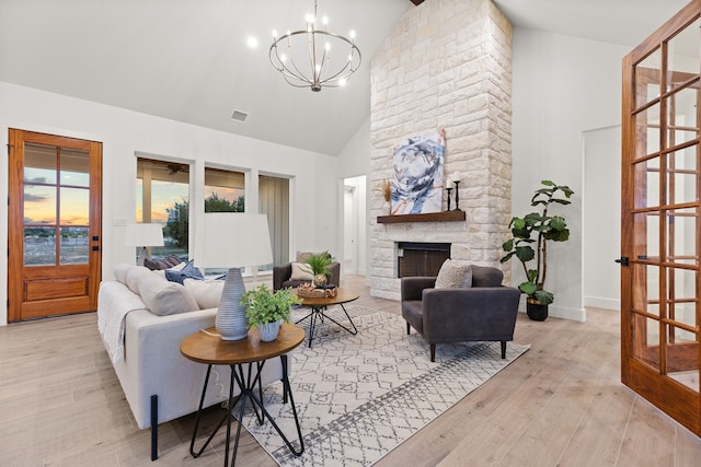 living room featuring high vaulted ceiling, a chandelier, a fireplace, and light hardwood / wood-style floors