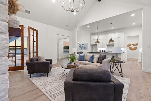 living room featuring high vaulted ceiling, a notable chandelier, light hardwood / wood-style floors, beam ceiling, and french doors