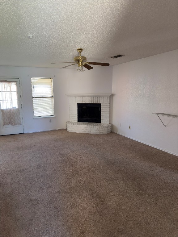 unfurnished living room featuring a textured ceiling, carpet, ceiling fan, and a fireplace