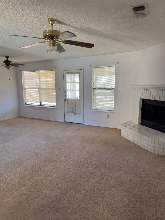 unfurnished living room with a brick fireplace, carpet, ceiling fan, and a textured ceiling