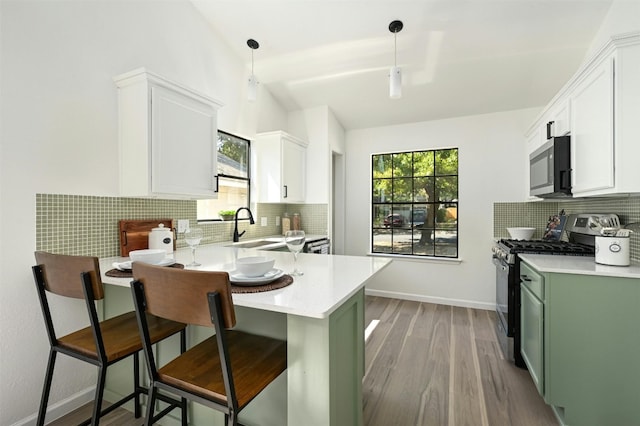 kitchen featuring a kitchen breakfast bar, stainless steel appliances, sink, green cabinetry, and hanging light fixtures