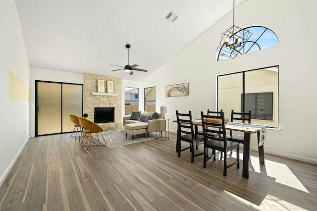 dining room with hardwood / wood-style flooring, high vaulted ceiling, a wealth of natural light, and a stone fireplace