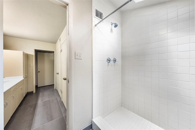 bathroom with tiled shower, vanity, and tile patterned flooring