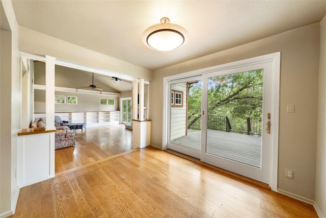 doorway to outside featuring decorative columns, ceiling fan, vaulted ceiling, wood finished floors, and baseboards