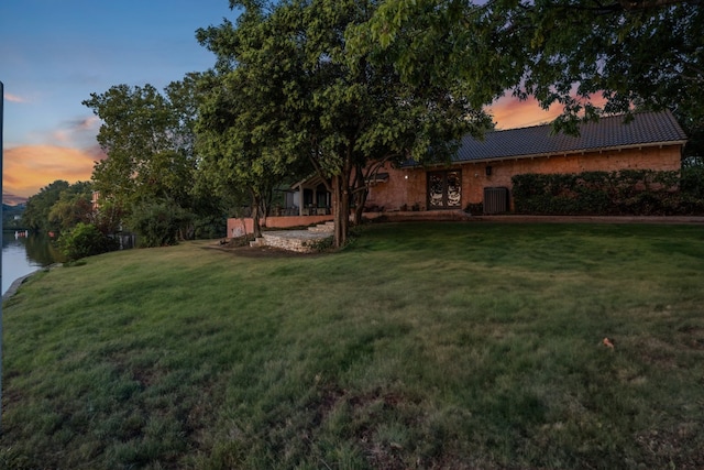 yard at dusk with a water view and central AC