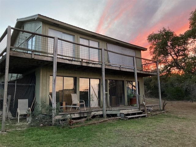 back house at dusk featuring a lawn and a deck