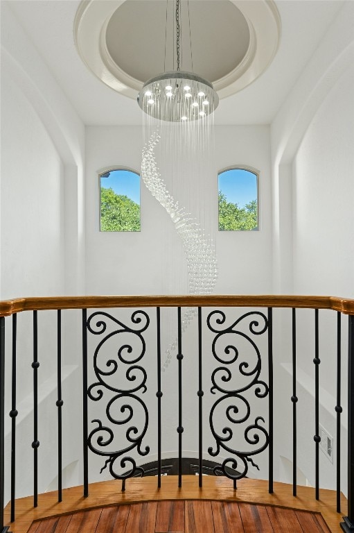 staircase with hardwood / wood-style floors, plenty of natural light, a raised ceiling, and an inviting chandelier