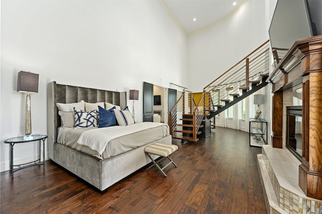 bedroom with a tile fireplace, a towering ceiling, and dark hardwood / wood-style floors