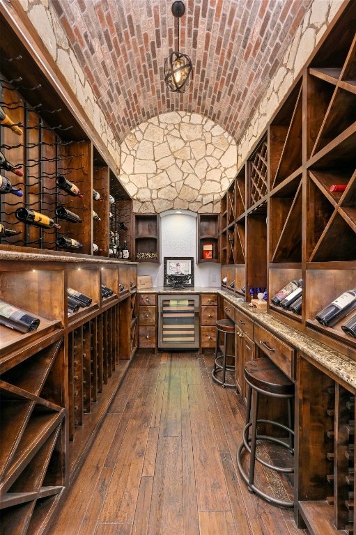 wine cellar featuring dark hardwood / wood-style flooring, brick ceiling, and wine cooler