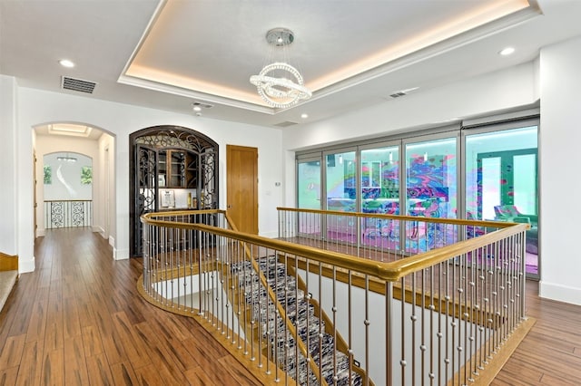 hallway with a tray ceiling, hardwood / wood-style floors, and an inviting chandelier