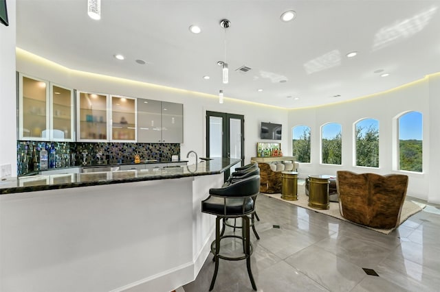 kitchen with a kitchen bar, backsplash, sink, dark stone countertops, and hanging light fixtures