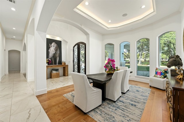 dining space with light wood-type flooring, crown molding, and a tray ceiling