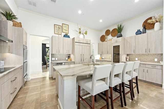 kitchen with ornamental molding, a breakfast bar, a kitchen island with sink, sink, and light brown cabinets