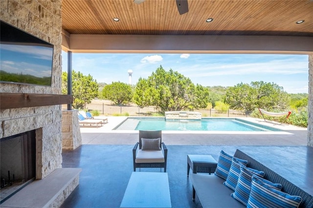 view of pool with a pool with connected hot tub, fence, an outdoor living space with a fireplace, a patio area, and a ceiling fan