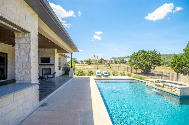 view of swimming pool featuring a pool with connected hot tub, an outdoor stone fireplace, a fenced backyard, and a patio area