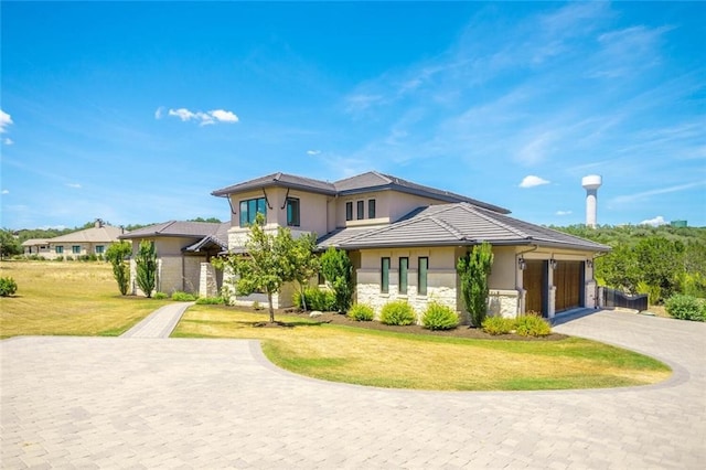 prairie-style home with a front lawn, stucco siding, a garage, stone siding, and driveway