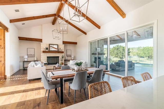 dining space with beam ceiling, high vaulted ceiling, wood finished floors, a fireplace, and a chandelier