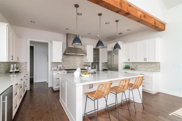 kitchen with dark wood-style floors, a center island with sink, light countertops, and wall chimney range hood