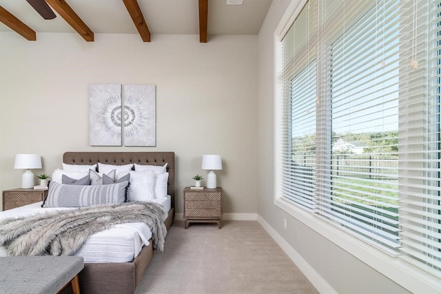 bedroom with beamed ceiling, light colored carpet, and baseboards