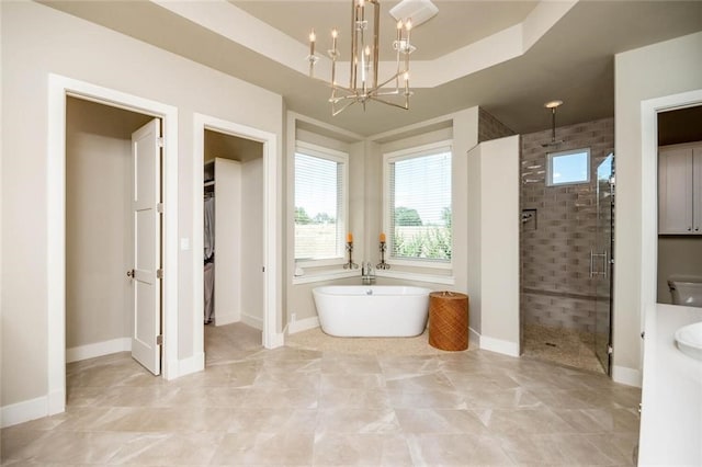 bathroom featuring an inviting chandelier, a stall shower, a freestanding bath, a spacious closet, and a raised ceiling