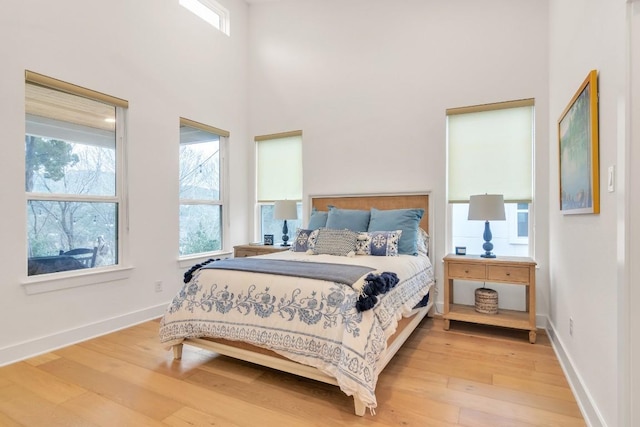 bedroom with wood-type flooring, multiple windows, and a high ceiling