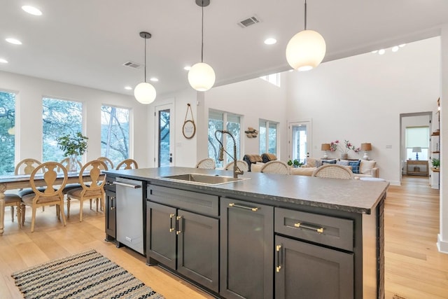 kitchen with a wealth of natural light, a kitchen island with sink, sink, pendant lighting, and light hardwood / wood-style flooring