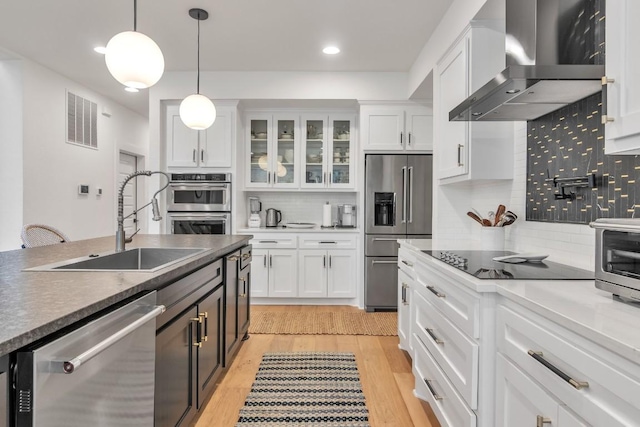 kitchen featuring white cabinets, appliances with stainless steel finishes, hanging light fixtures, and wall chimney range hood