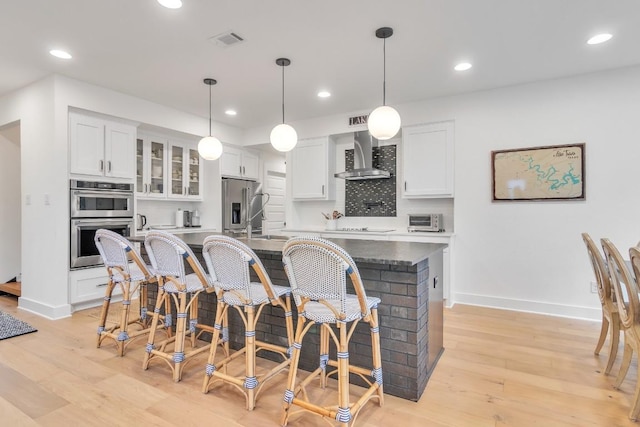 kitchen featuring white cabinets, a kitchen breakfast bar, wall chimney exhaust hood, an island with sink, and appliances with stainless steel finishes