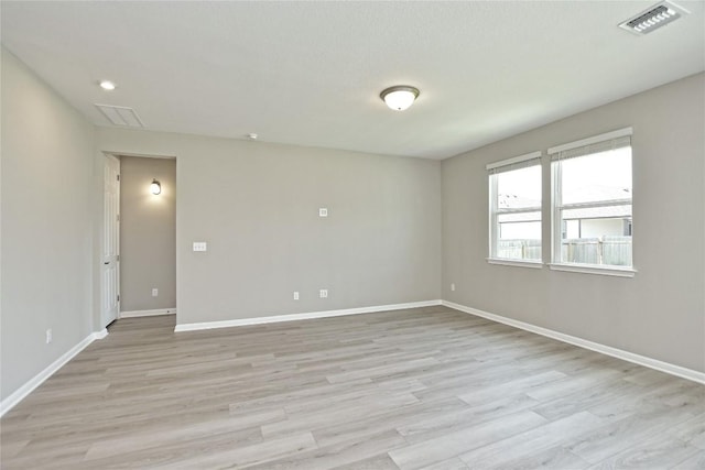 spare room with light wood-type flooring, visible vents, and baseboards