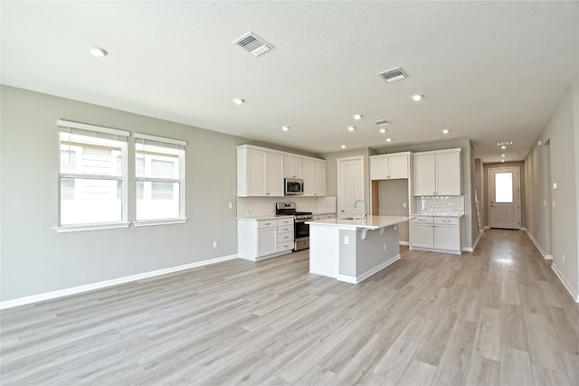 kitchen with stainless steel appliances, light hardwood / wood-style floors, sink, and an island with sink