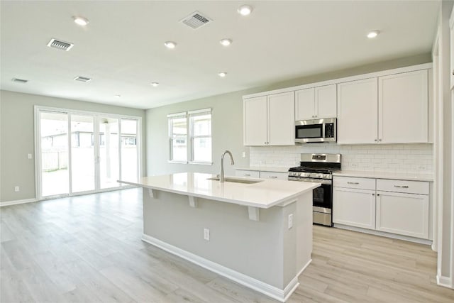 kitchen with light countertops, visible vents, appliances with stainless steel finishes, a kitchen island with sink, and a sink