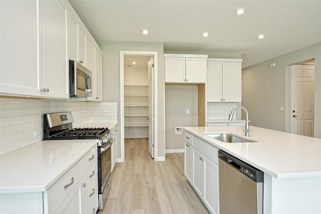 kitchen with stainless steel appliances, a sink, white cabinetry, light countertops, and a center island with sink