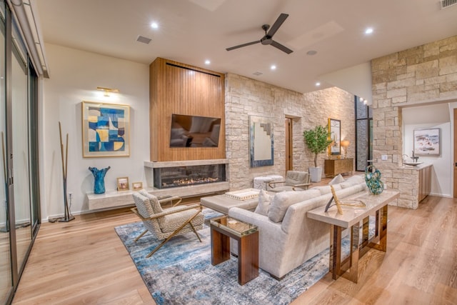 living room featuring ceiling fan, a stone fireplace, and light hardwood / wood-style flooring