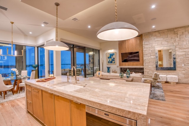 kitchen with pendant lighting, light wood-type flooring, light stone countertops, and sink