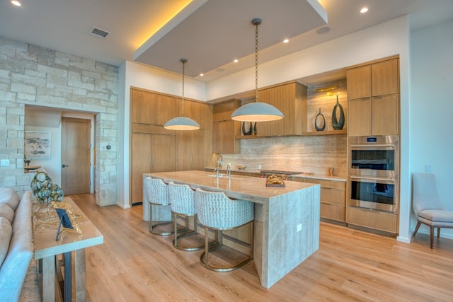 kitchen featuring light wood-type flooring, backsplash, pendant lighting, and stainless steel appliances