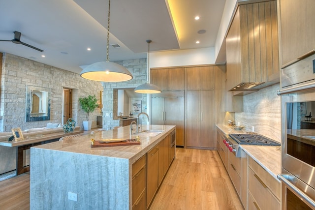 kitchen featuring hanging light fixtures, light hardwood / wood-style floors, a large island with sink, ceiling fan, and sink