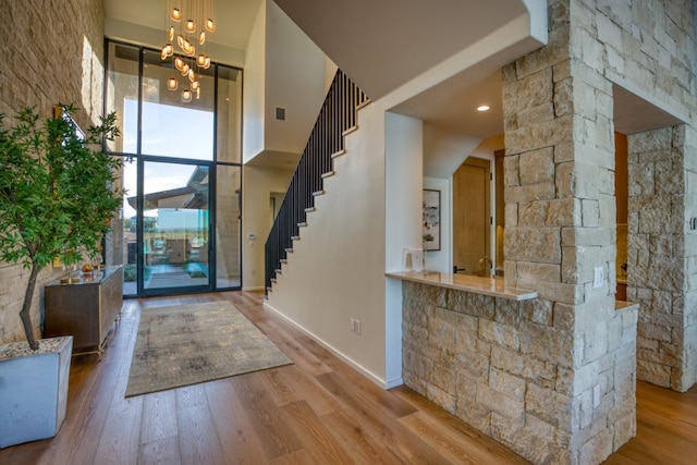 entryway featuring light wood-type flooring, a towering ceiling, and an inviting chandelier