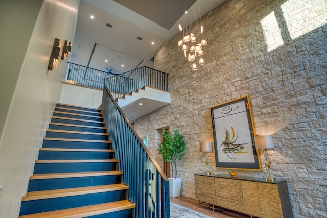 staircase with a notable chandelier, a towering ceiling, and hardwood / wood-style floors