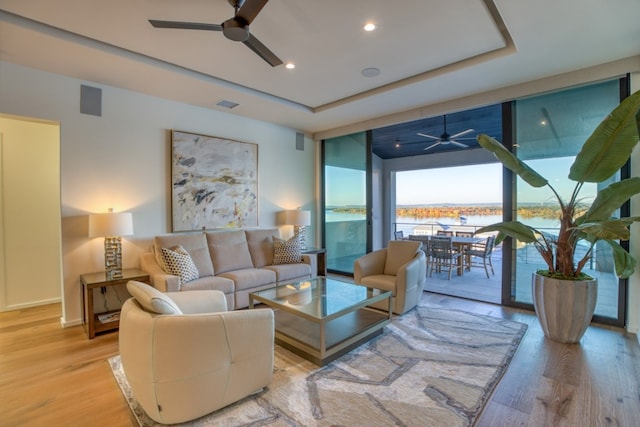 living room with ceiling fan, a wall of windows, light wood-type flooring, and a water view