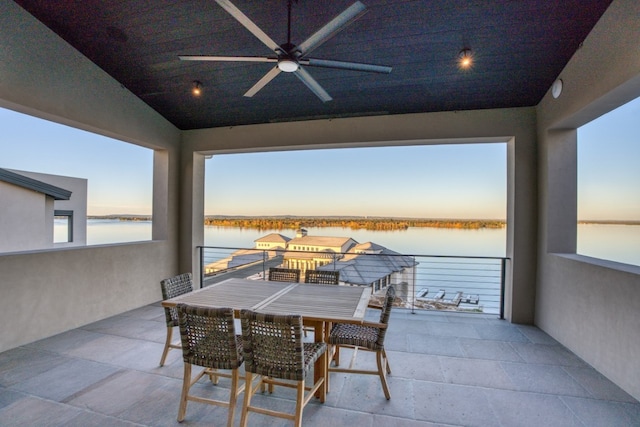 patio terrace at dusk featuring ceiling fan and a water view