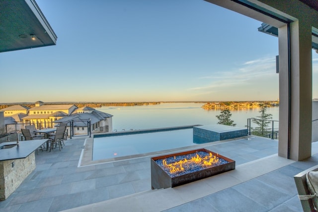 patio terrace at dusk featuring a fire pit and a water view