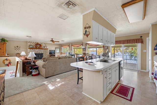 kitchen with ceiling fan, a stone fireplace, a kitchen island with sink, white cabinetry, and a breakfast bar