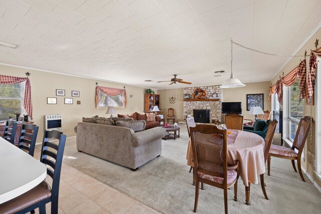 living room featuring heating unit, a stone fireplace, ceiling fan, ornamental molding, and light colored carpet