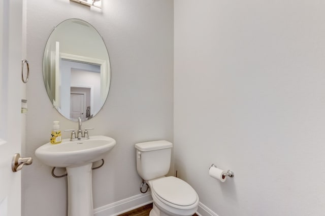 half bath featuring wood finished floors, a sink, toilet, and baseboards